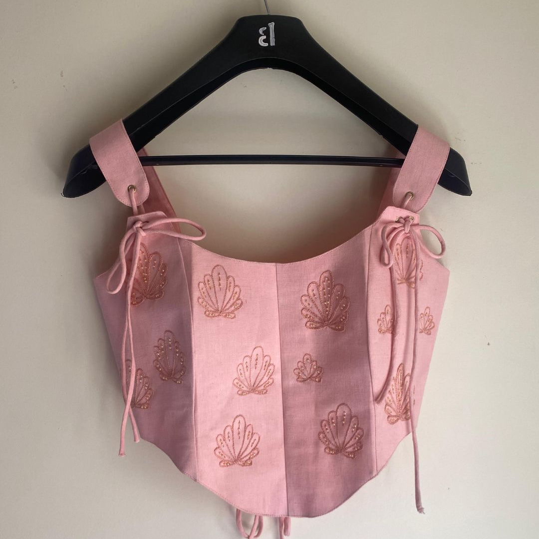 Pink top with shell patterns on a hanger against a white wall